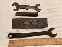 Photo showing four vintage metal hand tools on a white background with a ruler for scale: a flat blade plane, a wedge, and two wrenches.