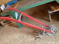 Side view of the vintage soil tiller showing red handles and metal wheel.
