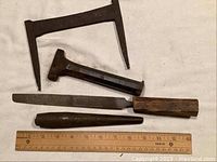 Four vintage metalworking hand tools: large frame tool, wedge, spike, and file with wooden handle on a white background