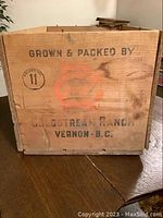 Front view of wooden crate showing branding with 'Grown & Packed By Coldstream Ranch Vernon BC' stamped on the side, some discoloration and stains visible.