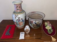 Lot with large painted Asian porcelain vase, ceramic planter with peacock design, small ginger jar, metal figurine on red fabric, and floral relief plaque on maroon backing.