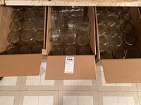 Top-down view of three open cardboard boxes filled with clear glass canning jars, some with rings.