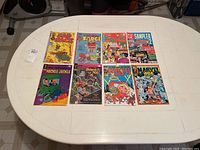 Top view of 8 comic books on white table including Sad Sack, Sarge, Reggie Me, Sampler, Heckle and Jeckle, Believe It or Not, Marvel Age.