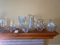 Wide view of all 7 crystal pieces on a wooden mantle, showing various sizes and shapes including 2 jugs and multiple bowls.