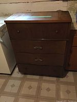 Four-drawer wood dresser with closed drawers, medium brown finish, showing some wear on top surface.