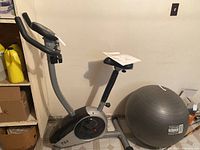 Upright magnetic exercise bike with gray and black frame next to gray exercise ball in basement storage area.