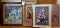 Four framed art prints leaning against a wall, showing a variety of floral and still life images in different frame styles and sizes.