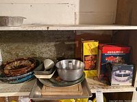 Shelf with stacked cookie sheet, baking pans, metal juicer, large steamer, trays, and boxed kitchen gadgets