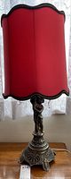 Full view of table lamp with red fabric shade and decorative figure base.