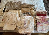 Photo showing folded assorted linens including tablecloths, napkins, sheets, and curtains in various neutral colors and fabrics.