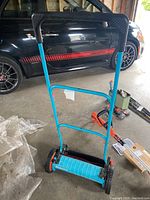 Full view of the blue Gardena 6000 SM manual lawn mower showing the black handle, orange wheels, and blue frame.