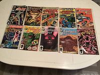 Full display of 10 Marvel comic books, all in plastic sleeves, laid out flat on a white surface showing front covers of titles including Fantastic Four and West Coast Avengers.