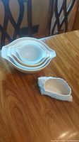 Photo of three white Pyrex nested ovenware dishes and textured seashell-shaped dish on wooden table