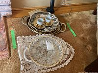 Silver plated trays, glass serving dish on lace mat, two porcelain cups on silver tray.