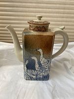 Full view of square-bodied ceramic coffee pot with handle, spout, lid and crane motif on front