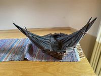 Angled side view of the canoe sculpture on a wooden table with a colorful cloth underneath.