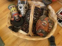 Woven basket containing five assorted painted masks of various designs and colors including animal and human faces