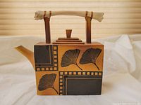 Front view of rectangular ceramic teapot showing brown and black leaf motifs and bone-style handle