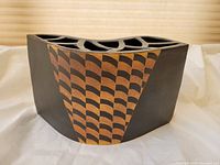 Side view showing geometric orange and black pattern on black ceramic surface.