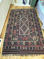 Full top-down view of entire kilim rug laid on hardwood floor next to dresser and bed.