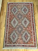 Full view of vintage Kilim rug with geometric diamond patterns on reddish background, showing overall design and fringed edges.