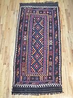 Full view of the hand-woven kilim rug showing geometric design and colors on a wood floor.
