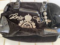 Black suede Juicy Couture handbag with embroidered crest, silver studs, and leather trim accents.