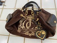 Full view of the Juicy Couture hand bag showing brown velvet fabric, leather handles, gold-tone hardware, and the large logo embroidery.