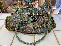 Front view showing overall shape, tapestry fabric with floral and geometric pattern, metal frame and beaded strap draped over bag