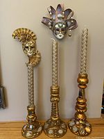 Three gold-toned decorative candlesticks with braided textured candles and mirror inset bases