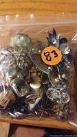 Clear plastic bag containing assorted costume jewelry items laid on a wooden surface.