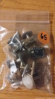 Plastic bag containing assorted tie tacs and cuff links including a black decorative cuff link and several metallic ones.