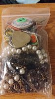 A clear plastic zip-lock bag filled with assorted costume jewelry including pearl-like strands, a heart-shaped pendant, and various chains and pendants.