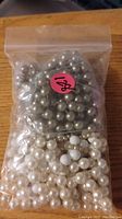 Photo of two sets of faux pearl necklaces, one set with large metallic grey beads in a resealable plastic bag, and the other set with smaller off-white faux pearls lying underneath the bag on a wooden surface.