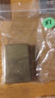 Photo of a vintage brass Zippo lighter showing wear and patina inside a clear plastic bag.