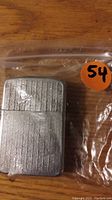 Silver tone metal lighter with vertical stripes in plastic bag with orange sticker showing number 54
