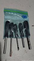 Five screwdrivers with black handles in a small sealed plastic bag, showing used condition and varying sizes.