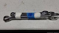 Four chrome finished combination wrenches taped together with worn paper tape showing size markings on white surface