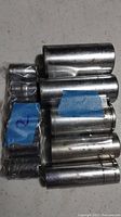 Various metal sockets in a pile, some labeled with blue tape, different sizes and shows surface wear and shine.