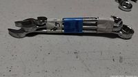 Photo of a set of 6 metal combination wrenches bound together by white and blue tape lying on a white surface.