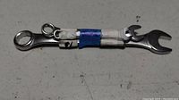 Metal combination wrench with box-end and open-end secured with blue and white tape shown on a light surface.
