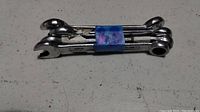Four metal combination wrenches stacked and bound with a blue band, placed on a speckled surface.