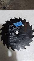Close up image of a black circular saw blade with teeth, marked The Challenger 7-1/4 inch, model CW714