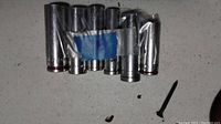 Photo shows 8 metal socket tools of various sizes held together by blue tape inside a plastic bag, laid on a white surface with a screw nearby.