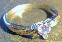 Close-up front view of a white gold ring showcasing the heart-shaped light amethyst center stone flanked by two small diamond chips.