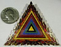 Photo showing front of triangular enamel pin next to a quarter for size reference.