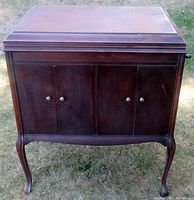 Full front view of the mahogany Victrola cabinet with closed doors, showing wood grain and curved legs.