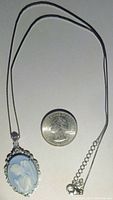 Full view of the sterling silver necklace with a blue and white praying angel pendant placed next to a quarter coin for size reference.