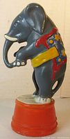 Side view of cast iron circus elephant still bank standing on red tub base showing paint details and condition