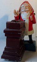 Front left angled view of cast iron Santa mechanical bank showing Santa, chimney and blue base, with some paint wear and chipping.